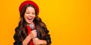 he image showcases a girl immersed in singing lessons in a room with a vibrant yellow wall in Hurstville, Sydney, Australia. The girl stands confidently, microphone in hand, ready to explore her vocal abilities. The room is adorned with musical elements, such as sheet music and a keyboard, creating an inspiring environment for learning. The girl's focused expression and poised posture reflect her passion and dedication to developing her singing skills. This image captures a moment of musical growth and artistic exploration as the girl embraces vocal lessons in Hurstville, Sydney, Australia.