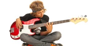 Kids guitar teacher near me, The image portrays a boy engaged in bass guitar lessons in a room with a white wall in Hurstville, Sydney, Australia. The boy sits comfortably, holding a bass guitar with confidence and focus. The room is neatly arranged with musical equipment, including amplifiers and music stands, creating a dedicated space for learning. The boy's determined expression and posture reveal his commitment to mastering the bass guitar. This image captures a moment of musical exploration and development as the boy embraces bass guitar lessons in Hurstville, Sydney, Australia.