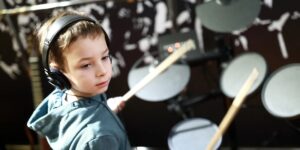 teacher drums lessons for kids, drums classes for kids, drums coach for kids, The image showcases a boy engaged in drum lessons in Hurstville, Sydney, Australia. Seated behind a drum set, he holds drumsticks and focuses intently on his rhythmic movements. The room is filled with the energetic beat of drums, creating an atmosphere of musical excitement. The boy's concentration and passion for drumming are evident in his determined expression. This image captures a moment of musical exploration and learning as the boy immerses himself in the world of drumming in Hurstville, Sydney, Australia.