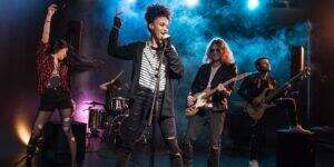 A vibrant scene unfolds on stage in Hurstville, Sydney, Australia. Five enthusiastic youngsters, all in their early teens, form a band as they practice what they have learned in their music lessons. Two girls take center stage, singing and dancing with passion and energy. On the left side, a music teacher strums a guitar, providing melodic support to the performance. To the right, a student confidently plays the bass guitar, while another student showcases their drumming skills at the back. The atmosphere is filled with youthful exuberance, collaboration, and the joy of making music together.